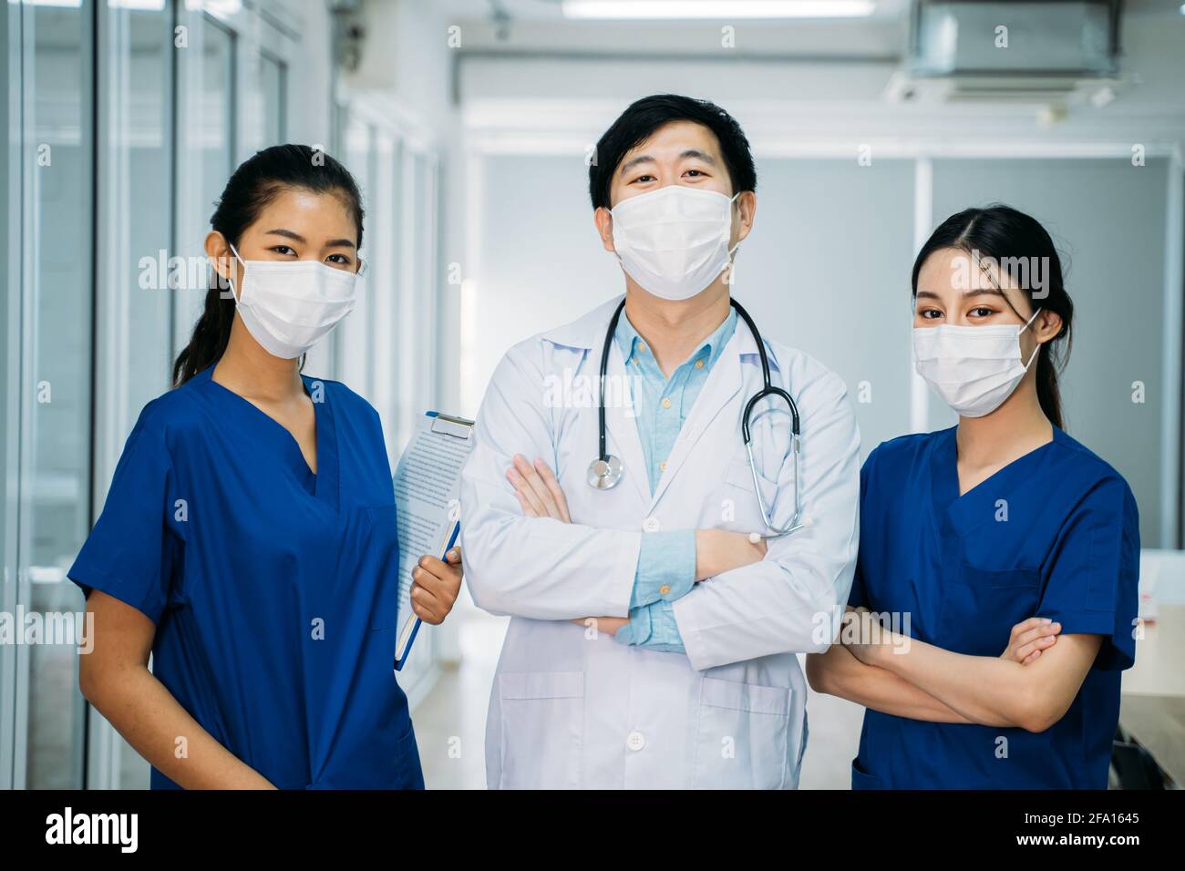 Portrait d'un groupe asiatique de médecins et d'infirmières en uniforme et en blouse de laboratoire avec stéthoscope et masque facial debout dans le passage de l'hôpital avec les bras croisés Banque D'Images