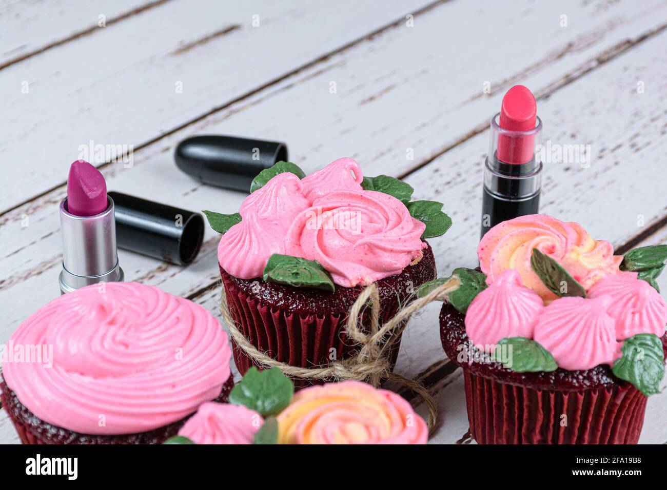 Cupcake en velours rouge avec glaçage à la crème au beurre. À côté de deux rouges à lèvres et autres petits gâteaux. Banque D'Images