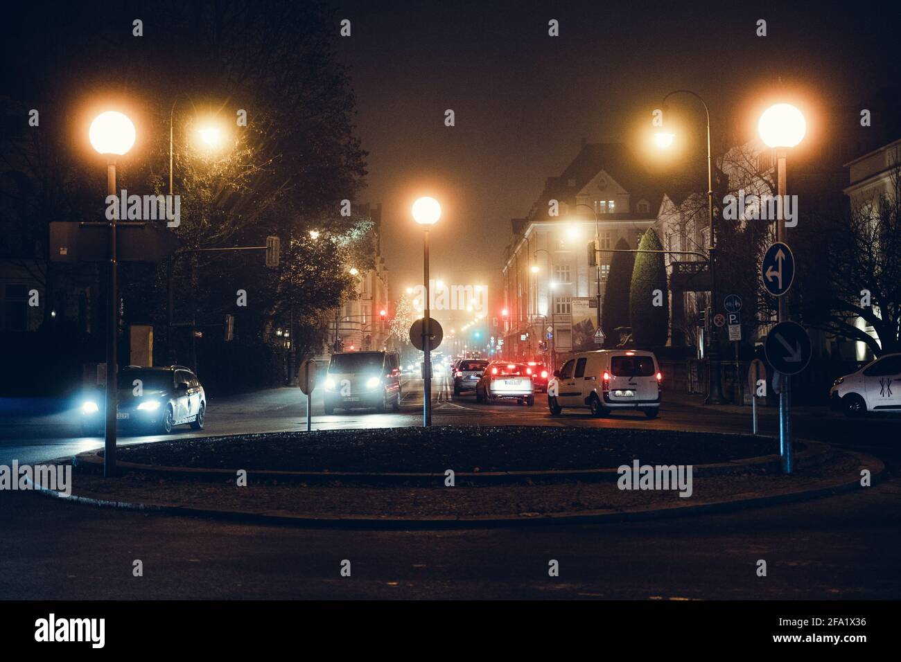 Avenue (route) pendant une nuit de pluie à Munich, Bavière, Allemagne. Panneaux de signalisation et rond-point. Les phares et les embouteillages éclairent la ville. Banque D'Images