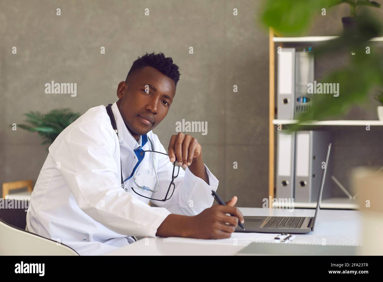 Médecin afro-américain professionnel de la santé assis à la table avec un ordinateur portable Banque D'Images