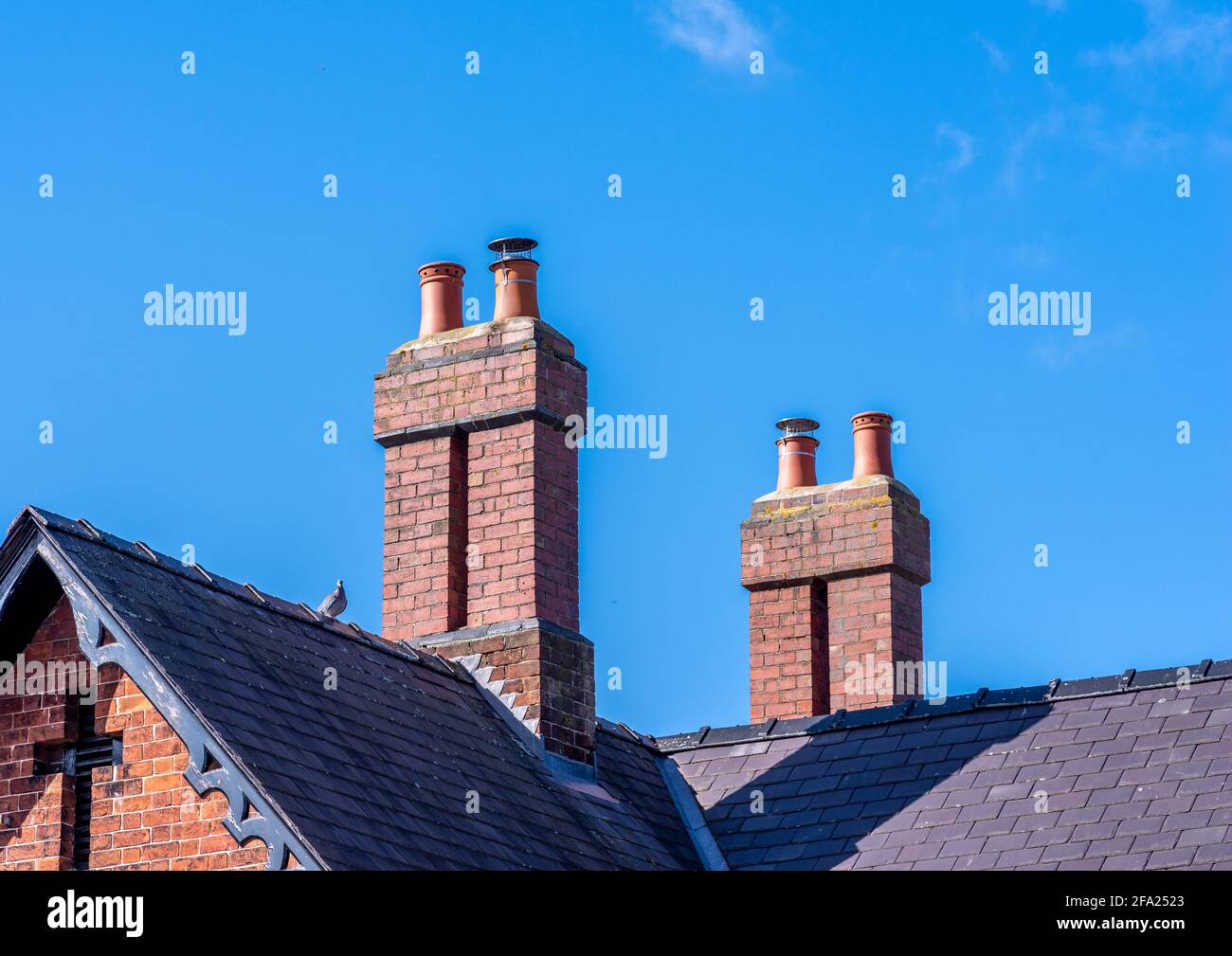 Chimys en briques rouges sur un toit en ardoise grise avec un fond bleu ciel par une journée ensoleillée Banque D'Images