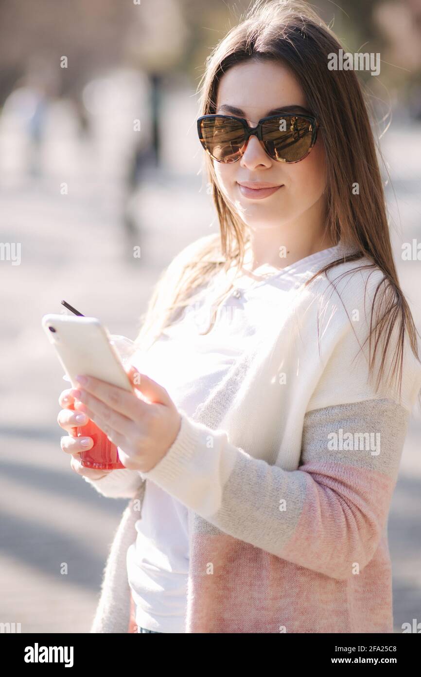 Belle femme utilisant le téléphone et boissons limonade à l'extérieur. Un jeune blogueur passe du temps dans le parc Banque D'Images