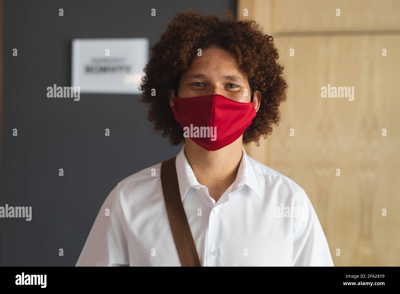 Portrait d'un homme de race mixte portant un masque de visage debout hall de l'hôtel avec sac à bandoulière Banque D'Images