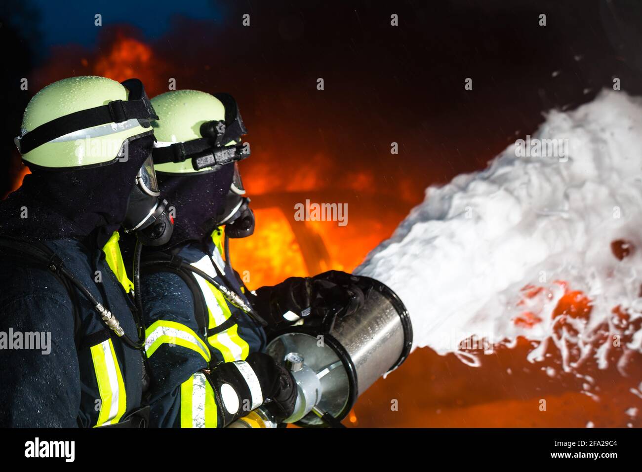 Pompiers pompier - extinction d'un grand brasier, ils sont debout avec des vêtements de protection en face de mur de feu Banque D'Images