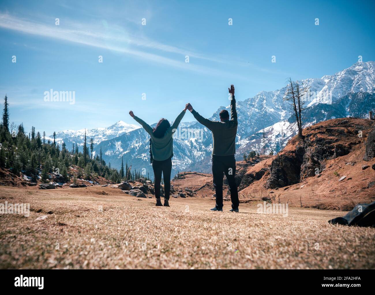 Vue arrière des voyageurs avec les mains levées face à un paysage de montagne pittoresque, Kothi Meadows, Manali, Inde Banque D'Images