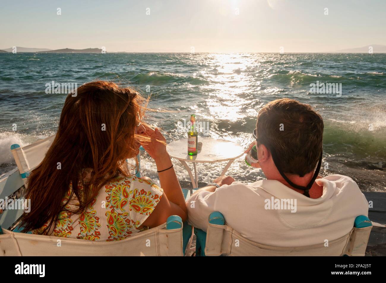 Un couple assis au bar de la plage avec une bière À la main en regardant le coucher du soleil à Mykonos Grèce Banque D'Images