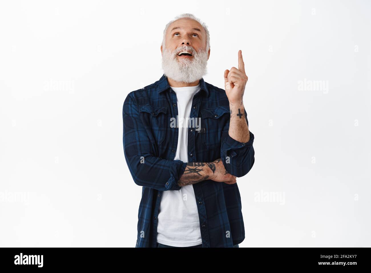 Grand-père élégant et cool avec tatouages et barbe longue, regardant et pointant le doigt vers le haut de la publicité, regardant au-dessus de l'espace publicitaire de texte promotionnel Banque D'Images