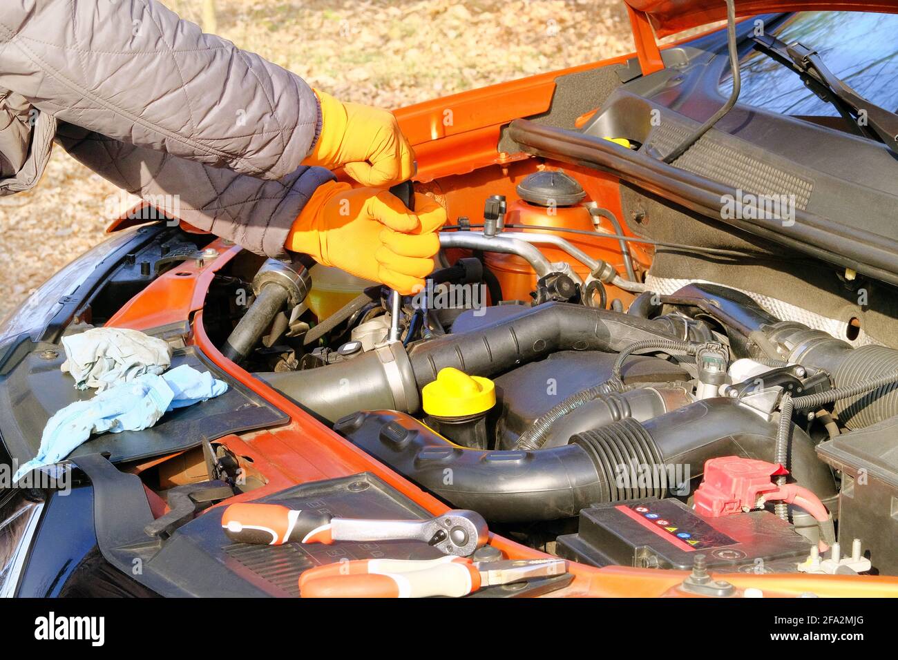 Les mains du conducteur dans des gants en caoutchouc orange vérifient la voiture, ouvrent le capot. Voitures et transport, gros plan. Problèmes avec la voiture sur route pendant les déplacements. Banque D'Images