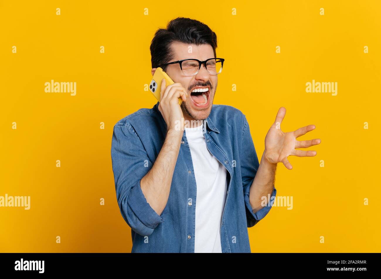 Conversation téléphonique désagréable. Un jeune homme caucasien irrité et furieux hurle pendant une conversation téléphonique, en faisant des gestes avec la main, se tient sur un fond orange isolé Banque D'Images