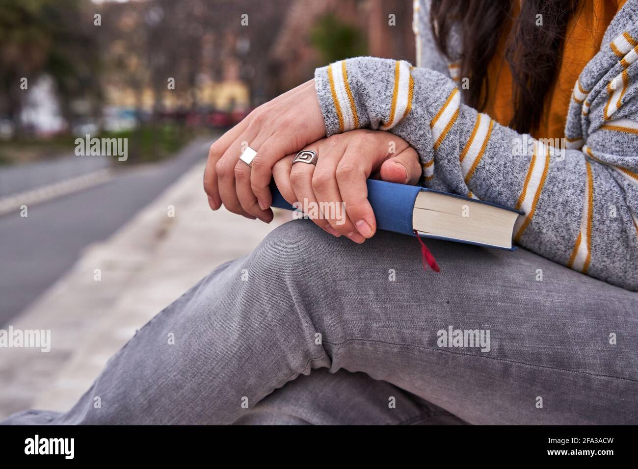 Mains croisées avec des anneaux dans ses doigts sur livre fermé. Section médiane de la dame assise dans un parc tenant le livre sur ses jambes. Connaissance et lecture c Banque D'Images