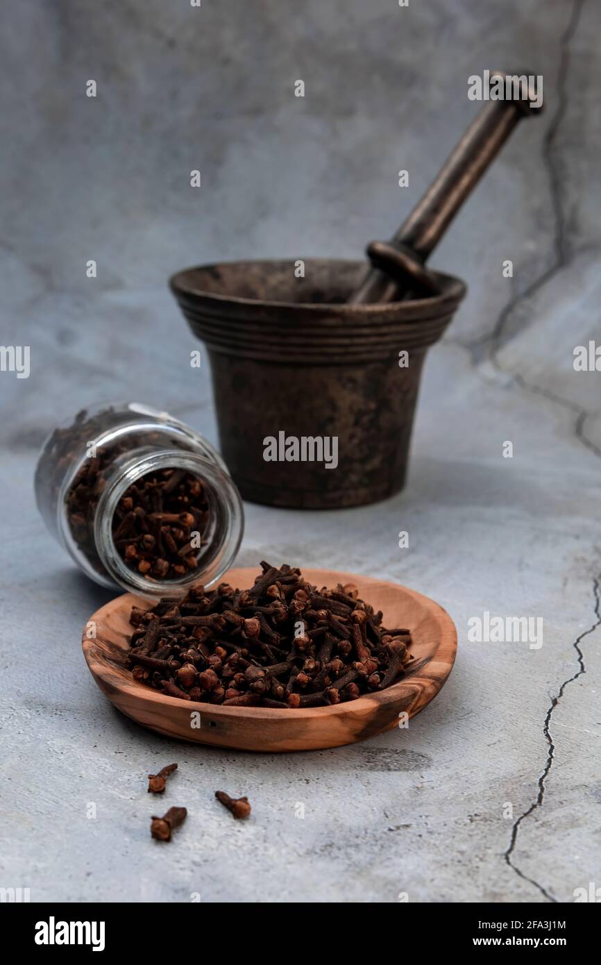 Métal Mortar pour pigeons et clous de girofle dans une plaque en bois.les clous de girofle sont les boutons de fleurs aromatiques d'un arbre de la famille des Myrtaceae, Syzygium aromaticum. Banque D'Images