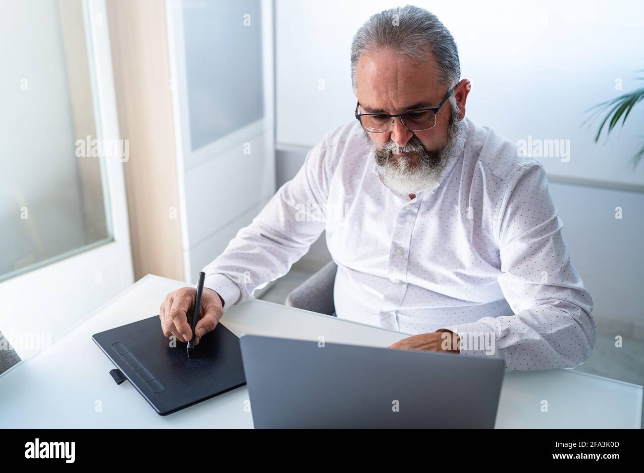 Homme senior barbe travaillant avec un ordinateur portable et une tablette dans son bureau Banque D'Images