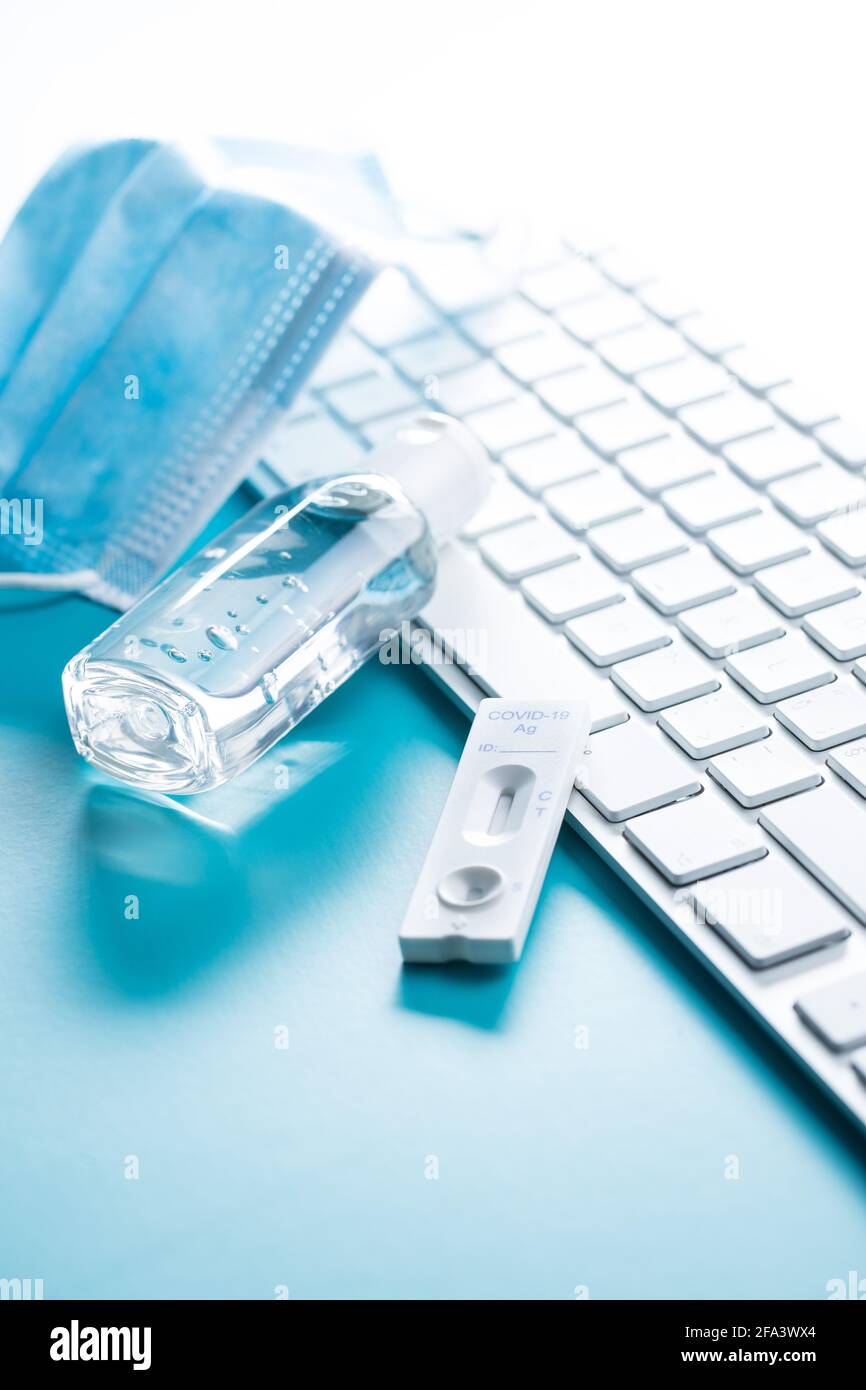 Test d'antigène rapide Covid-19. Kit de test rapide des anticorps, masque chirurgical et clavier d'ordinateur sur fond bleu. Banque D'Images