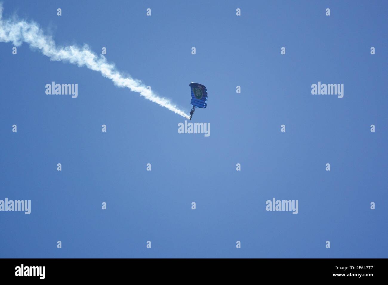 L'équipe d'exposition de parachutistes Red Devils descend avec une longue fumée Sentier au-dessus des terrains d'entraînement militaire de la plaine de Salisbury, sous un terrain sans nuages ciel bleu vif Banque D'Images