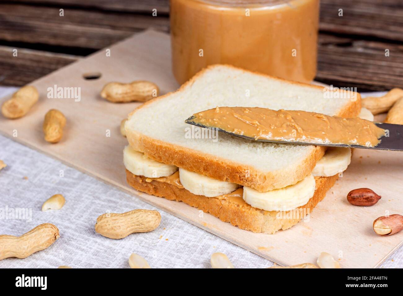 Sandwich maison pour le petit-déjeuner avec beurre d'arachide frais et croquant et bananes sur fond textile léger. Banque D'Images