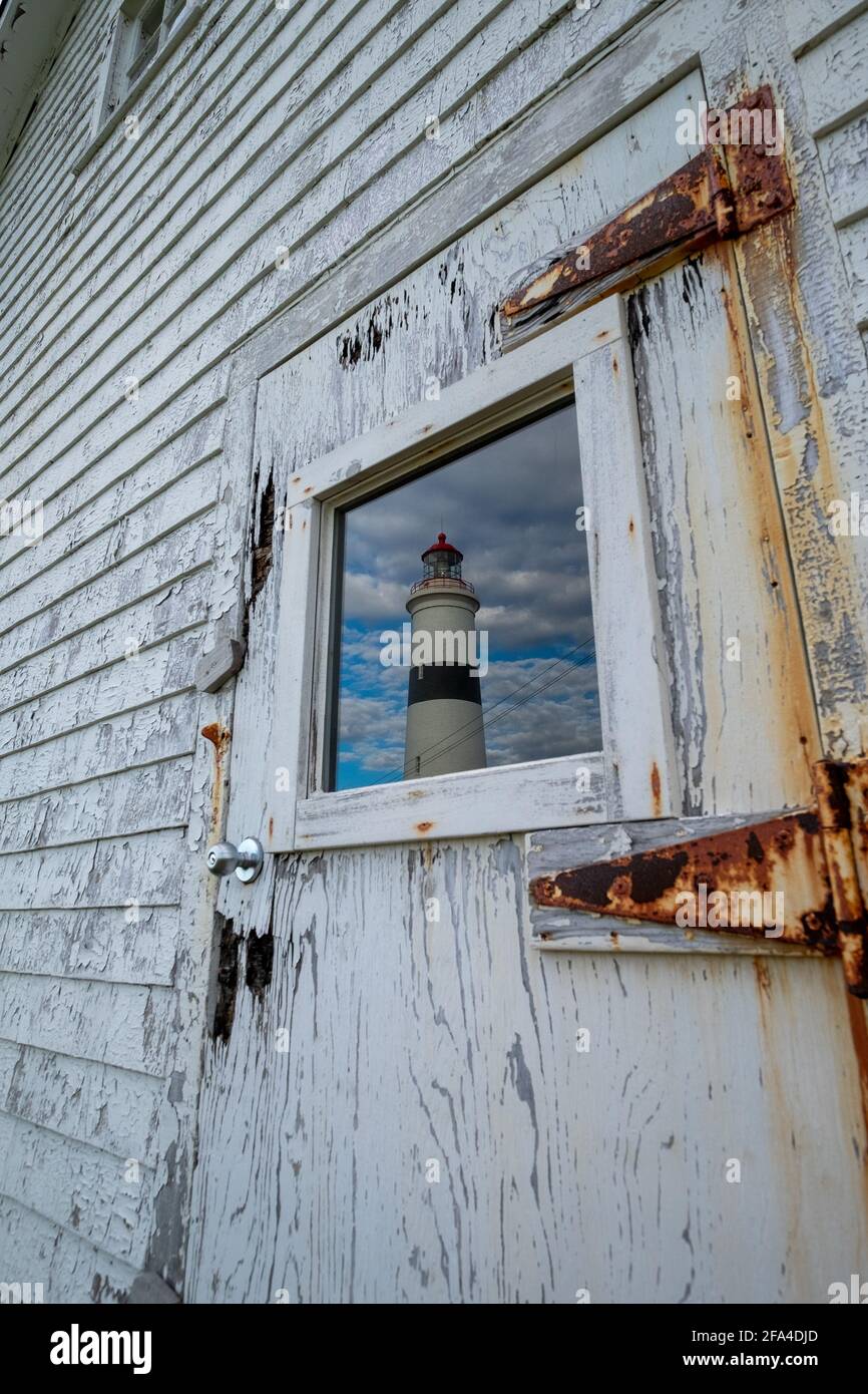 Un mur extérieur en bois usé blanc avec un panneau étroit. Au centre du mur, il y a une fenêtre en verre avec un reflet d'un phare. Banque D'Images