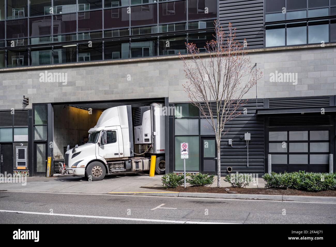 Semi-camion commercial blanc à cabine de jour avec toit le becquet et la semi-remorque du réfrigérateur font une livraison dans un espace très restreint pour le magasin local Banque D'Images