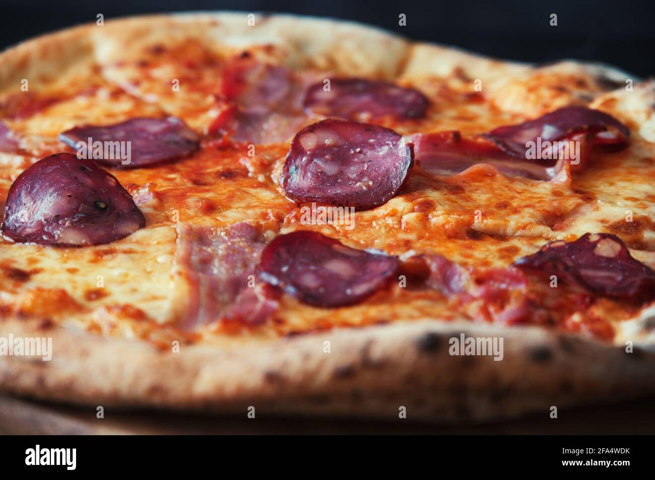Délicieuse pizza maison sur une assiette en bois contre le noir arrière-plan Banque D'Images