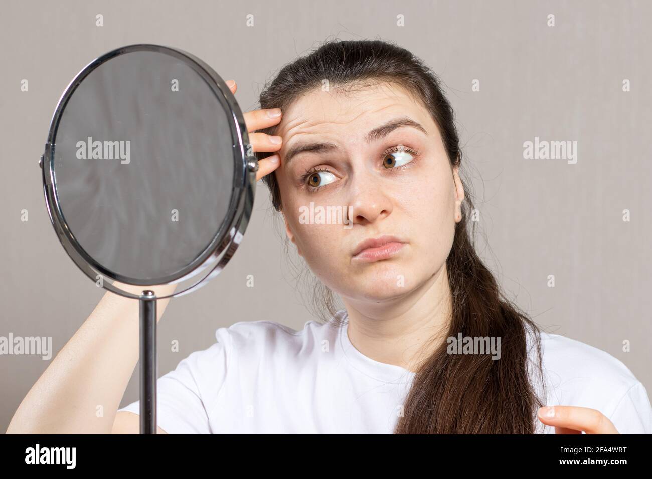 Une jeune femme regarde dans le miroir et voit les premières rides. Soins de la peau du visage anti-âge en cosmétologie et en dermatologie Banque D'Images