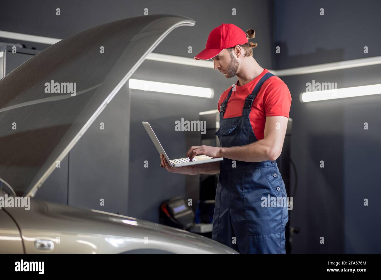 Homme regardant l'ordinateur portable près du capot de voiture ouvert Banque D'Images