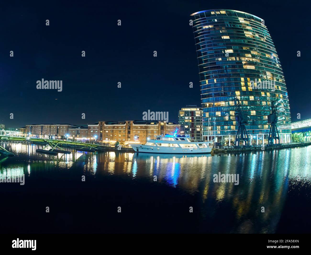 Un gratte-ciel de Canary Wharf, tournoyé et déformé par une lentille Fish-eye, avec des lumières flamboyantes, le tout reflété dans les eaux fixes du quai. Banque D'Images
