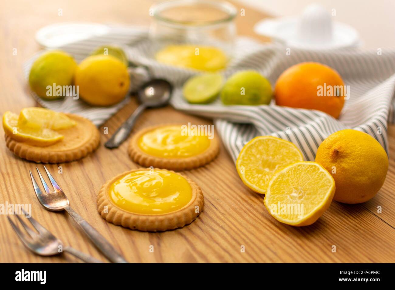 Quelques petits gâteaux frais cuits ou des gâteaux au citron, des ingrédients sur une table en bois comme des citrons, des oranges, des limes. Fourchettes et cuillères prêtes à être utilisées. Banque D'Images