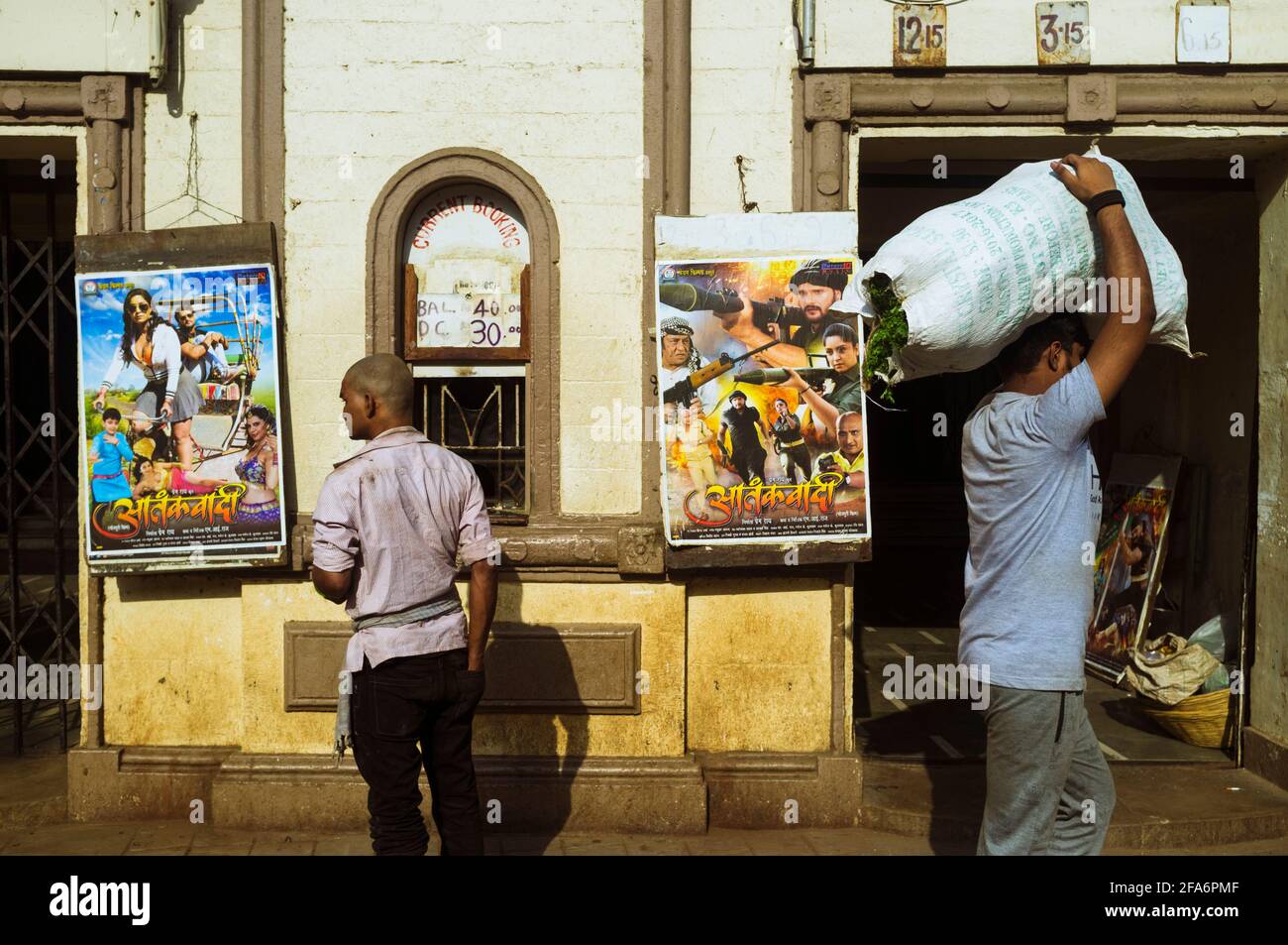 Mumbai, Maharashtra, Inde : deux hommes marchent devant un petit théâtre de cinéma jouant des films Bollywood dans le quartier de Byculla. Banque D'Images