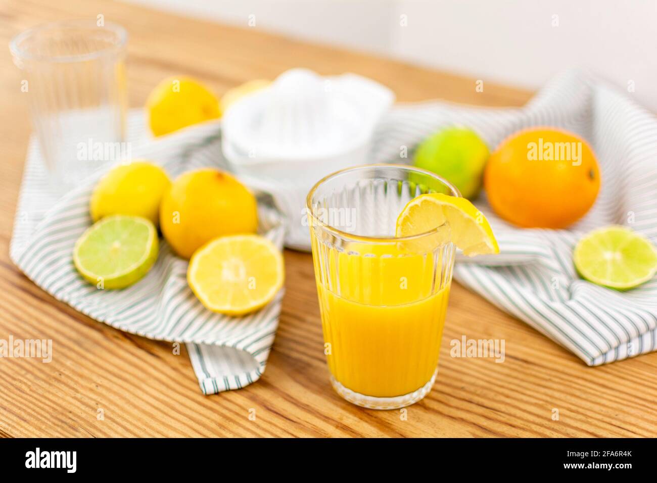 Un verre de jus d'orange frais sur une table en bois avec des agrumes comme des citrons, des oranges, des limes et une serviette de cuisine. Banque D'Images