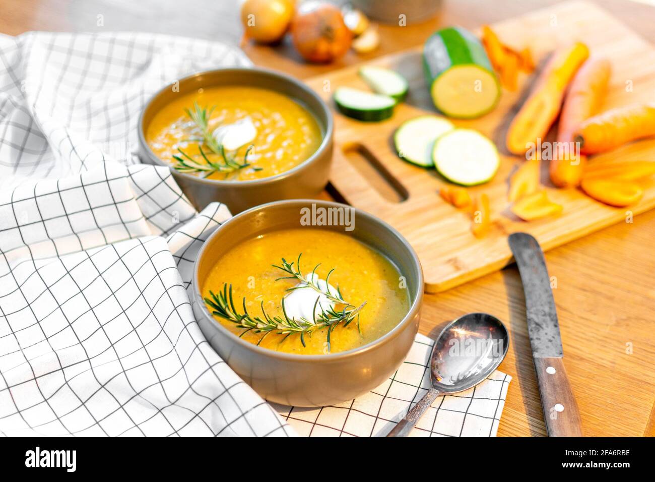 Un bon repas maison contenant une soupe de légumes frais avec des carottes et des courgettes et des oignons servis sur une vieille table en bois avec beaucoup de garniture. Banque D'Images