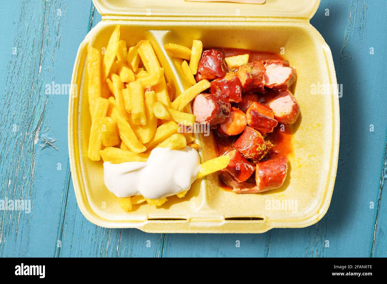 directement au-dessus de la vue sur le currywurst et les frites avec de la mayonnaise dans une boîte à emporter sur une table en bois Banque D'Images