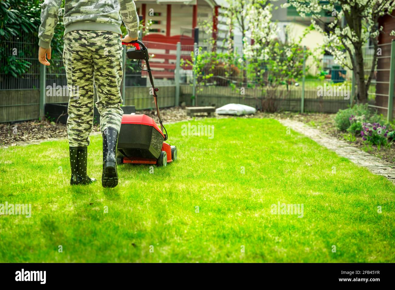 Entretien de pelouse - adolescent coupant la pelouse dans le petit jardin avec tondeuse électrique Banque D'Images