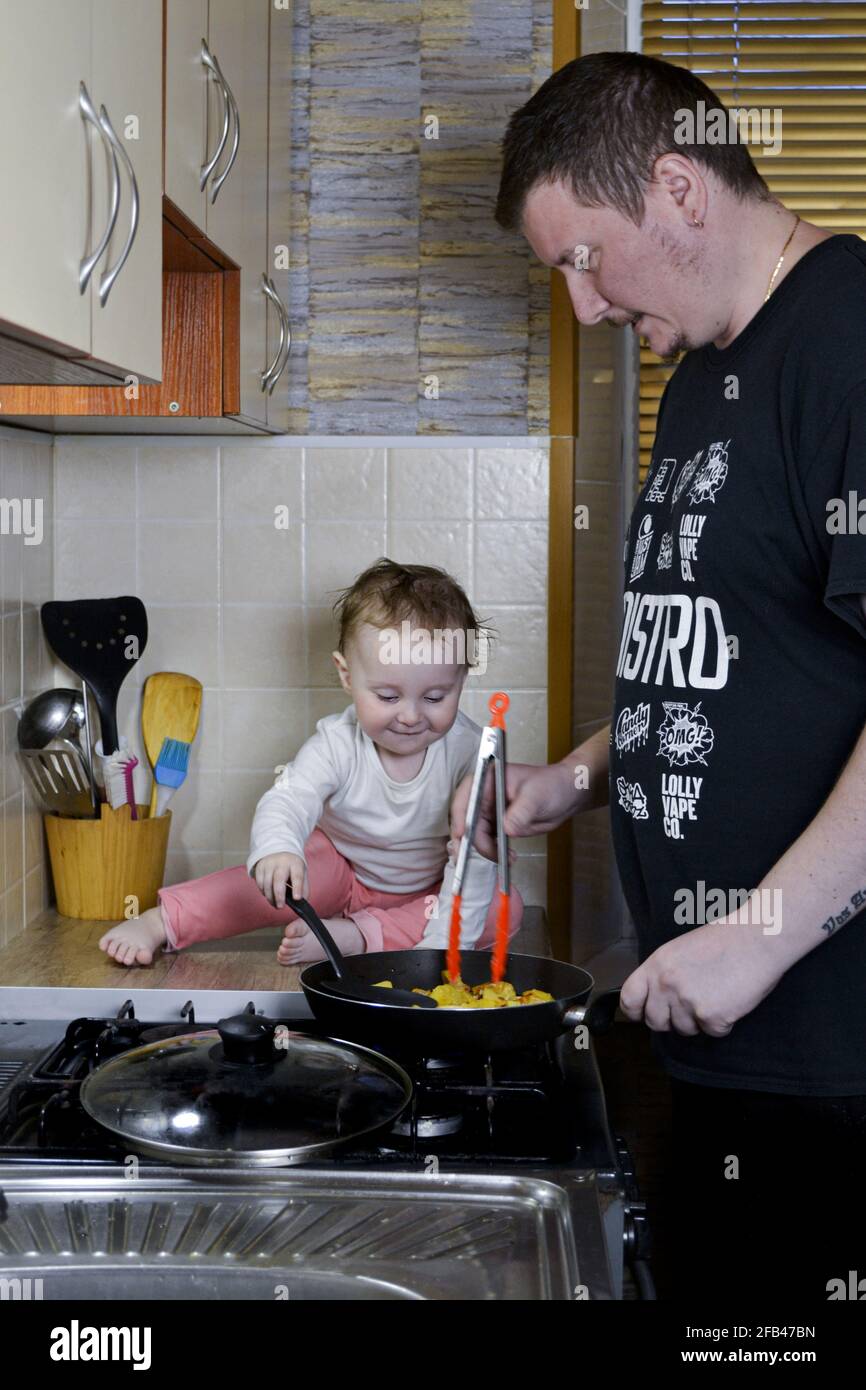 petite fille aidant papa à cuisiner en s'asseyant dans la cuisine tableau Banque D'Images