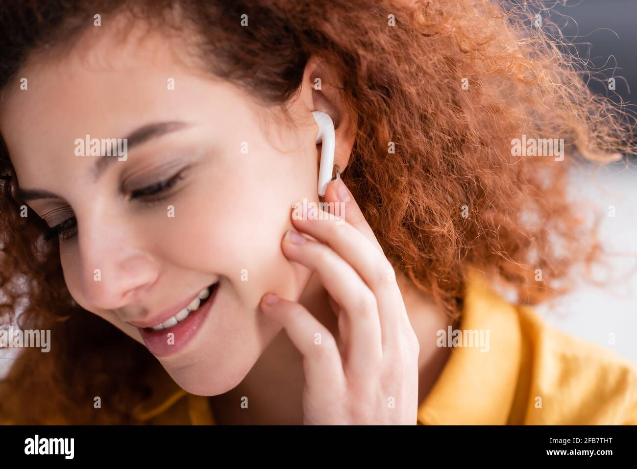 une femme heureuse avec des cheveux ondulés qui ajustent les écouteurs tout en écoutant de la musique à la maison Banque D'Images