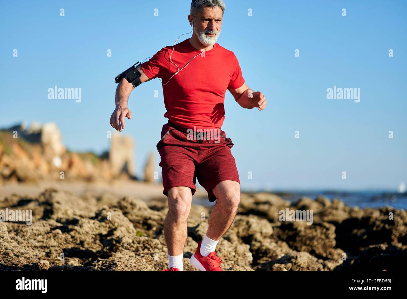 Homme courant à travers des rochers sur la plage pendant la journée ensoleillée Banque D'Images