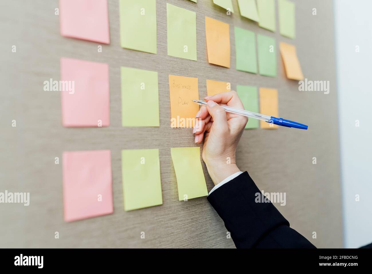 Une femme entrepreneur écrit sur des notes adhésives fixées sur un mur beige Banque D'Images