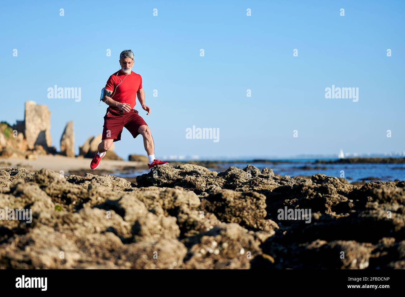 Homme mature qui court sur des rochers à la plage Banque D'Images