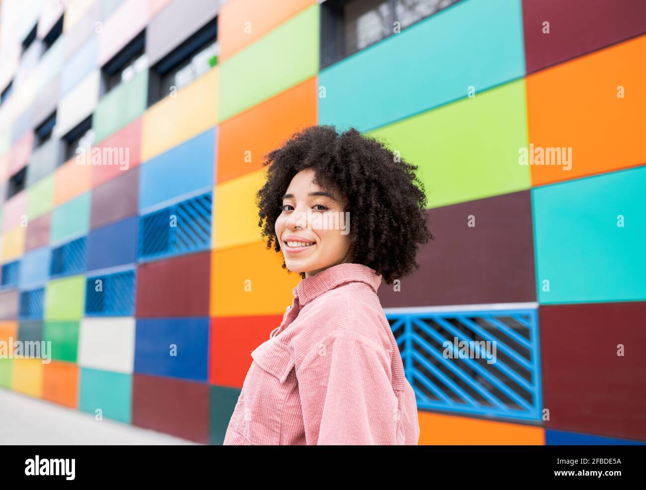 Femme en cheveux bouclés souriant dans un bâtiment coloré Banque D'Images