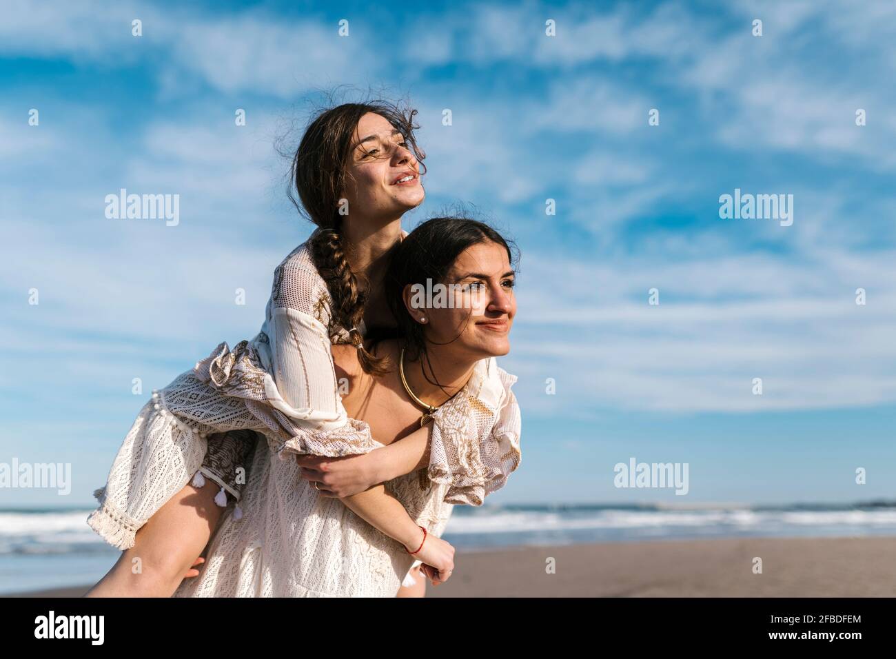 Une jeune femme qui regarde loin tout en dorant une amie à la plage Banque D'Images