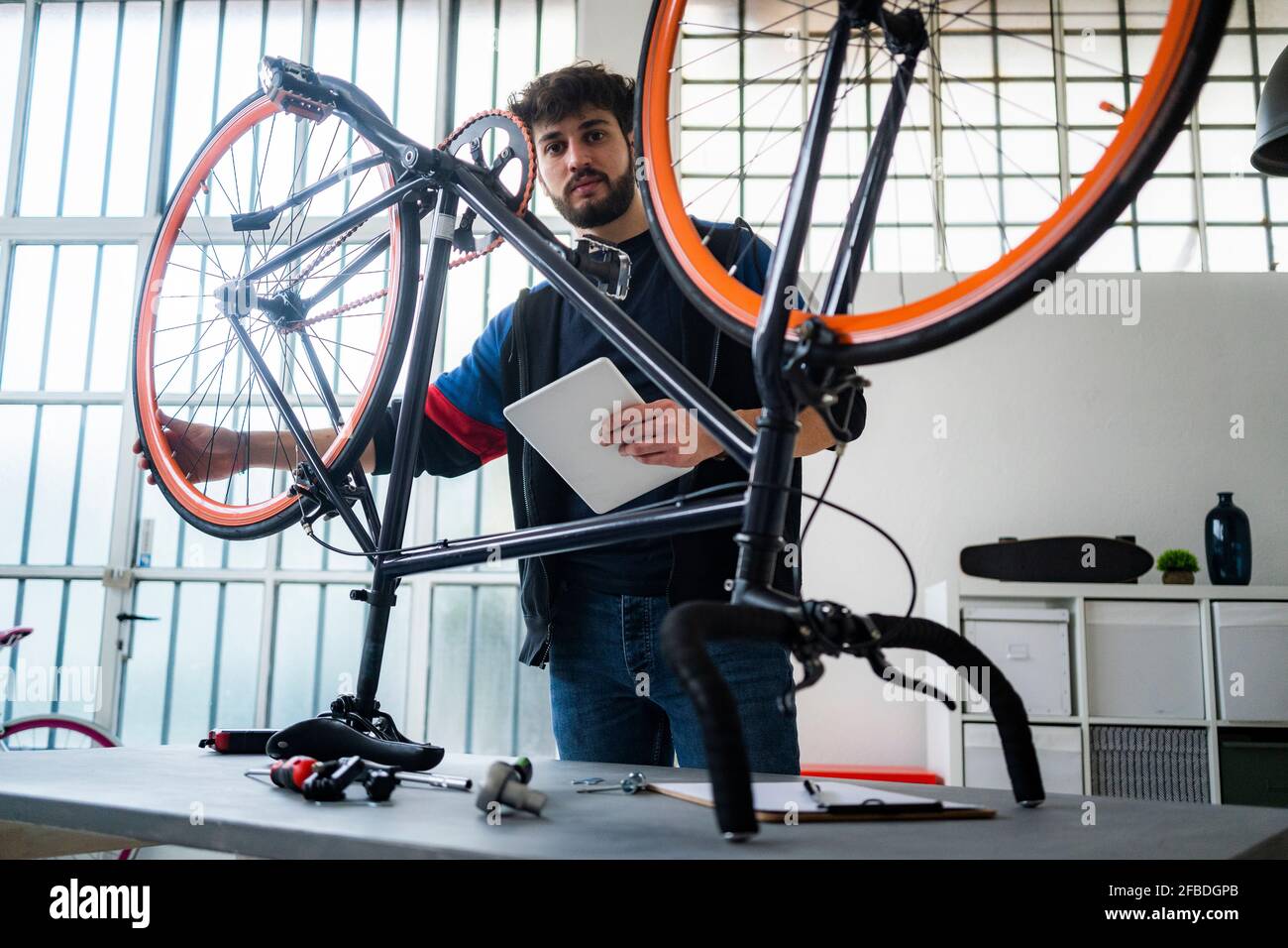 Homme avec tablette numérique tenant la roue de vélo à la maison Banque D'Images