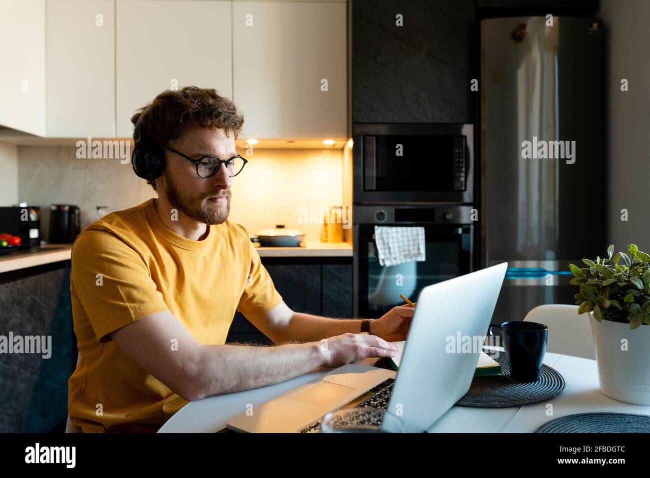 Un travailleur indépendant est un homme qui écoute des écouteurs tout en utilisant un ordinateur portable cuisine Banque D'Images
