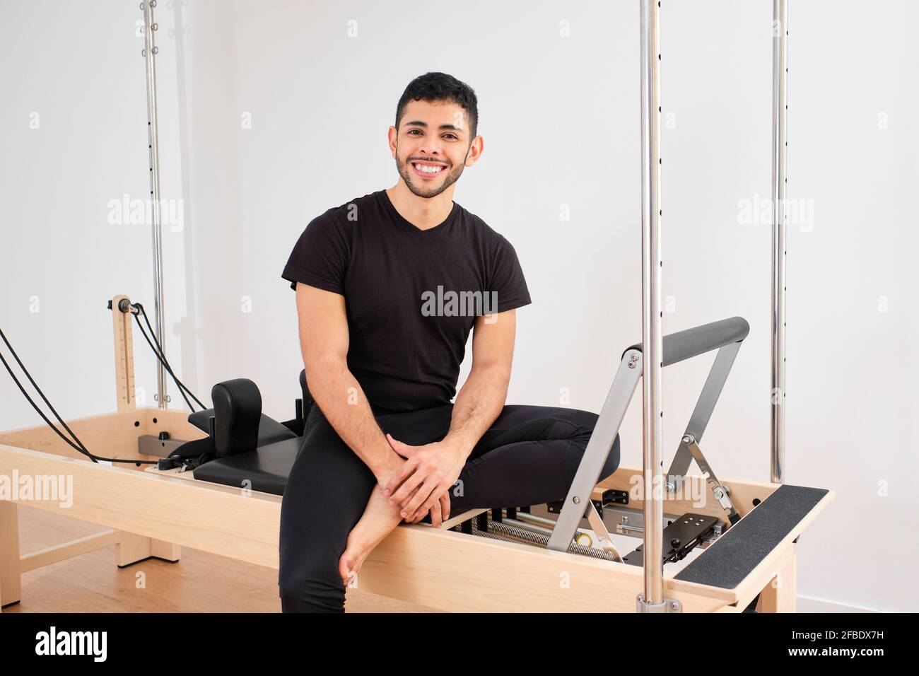 Homme souriant assis sur la machine à pilates dans la salle de conditionnement physique Banque D'Images