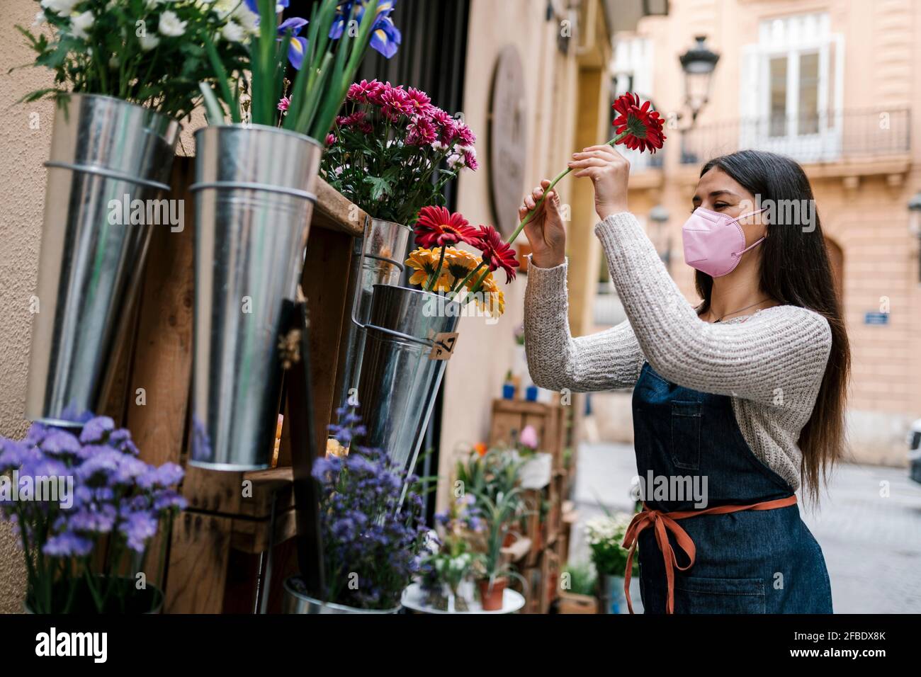 Jeune fleuriste femelle avec masque de protection pour le visage Gerbera Daisy fleur en magasin Banque D'Images