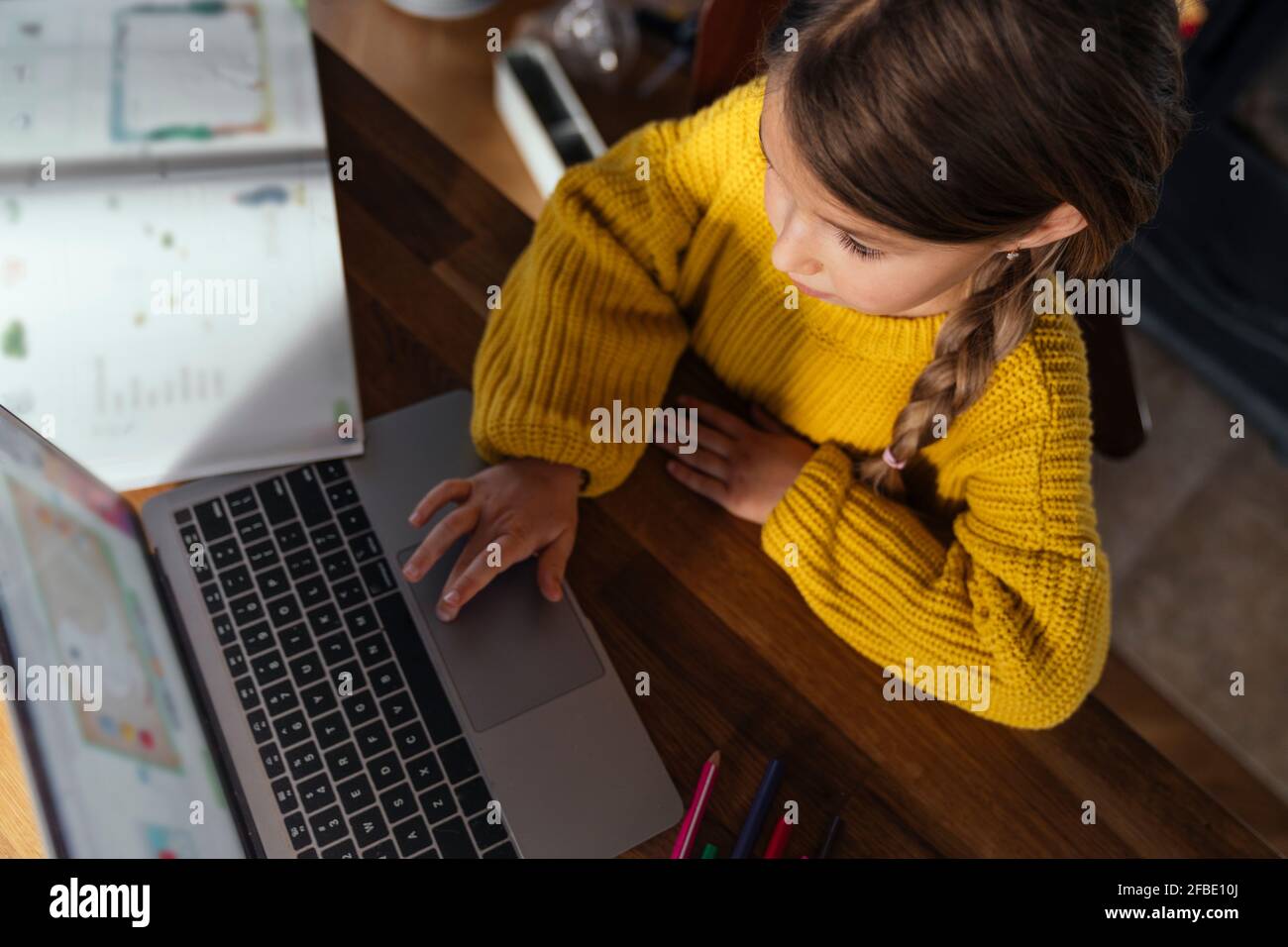 Fille en chandail jaune e-learning par ordinateur portable à la maison Banque D'Images
