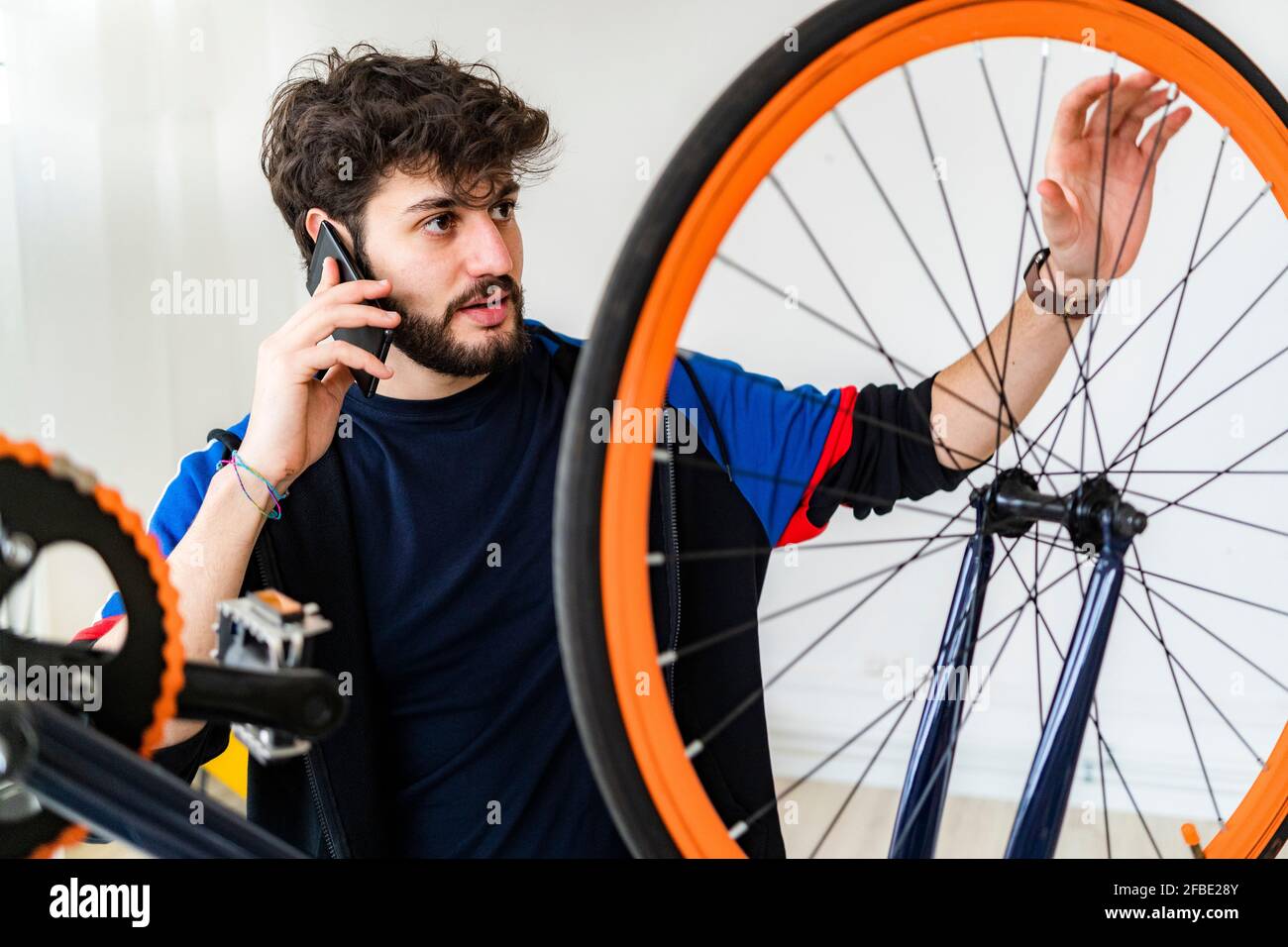 Homme parlant sur smartphone tout en examinant la roue de vélo à accueil Banque D'Images