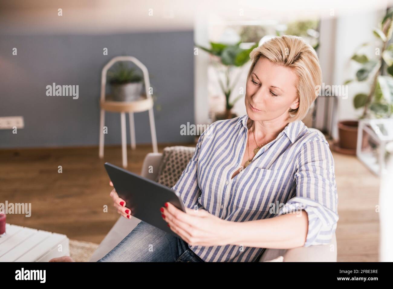 Femme mature utilisant une tablette numérique tout en étant assise sur un canapé séjour Banque D'Images