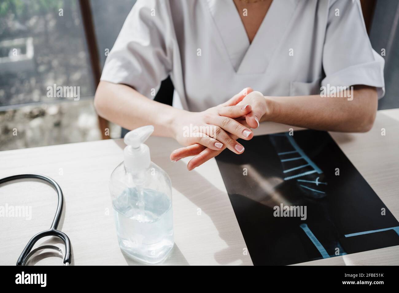 Une femme médecin se frottant les mains ensemble tout en appliquant de l'assainisseur au bureau Banque D'Images