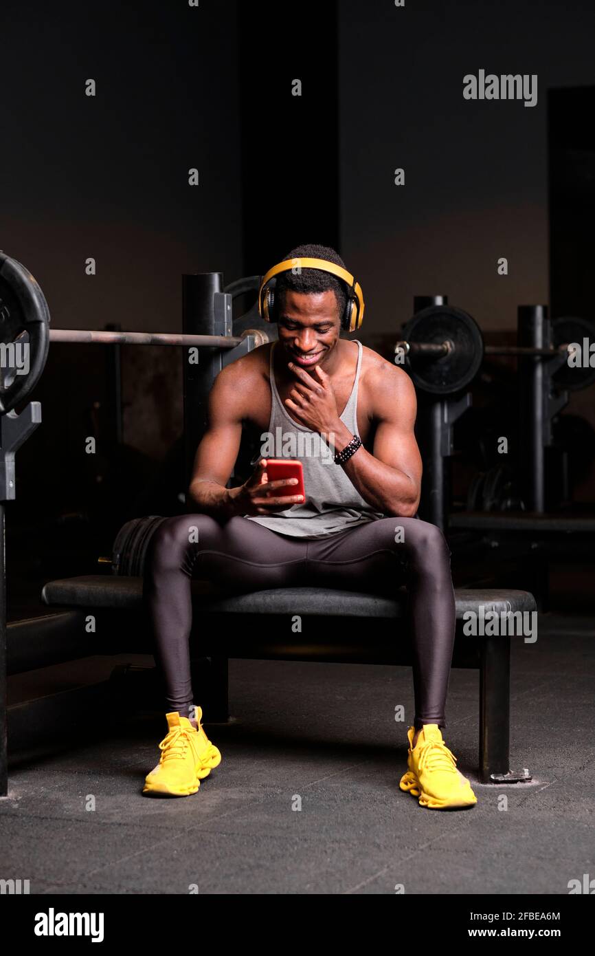 Souriant jeune africain avec des écouteurs utilisant un smartphone à salle de sport Banque D'Images