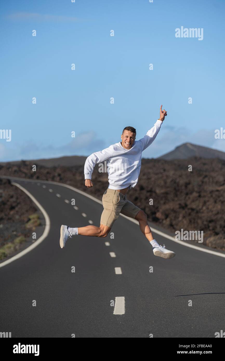 Souriant, un homme touristique se fait des gesticulations et saute sur la route Banque D'Images