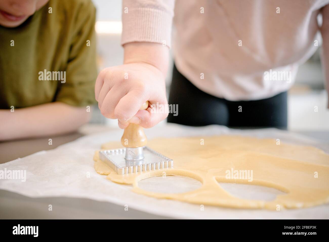 Fille utilisant un emporte-pièce à poignée en bois sur la pâte dans la cuisine tout en regardant Banque D'Images