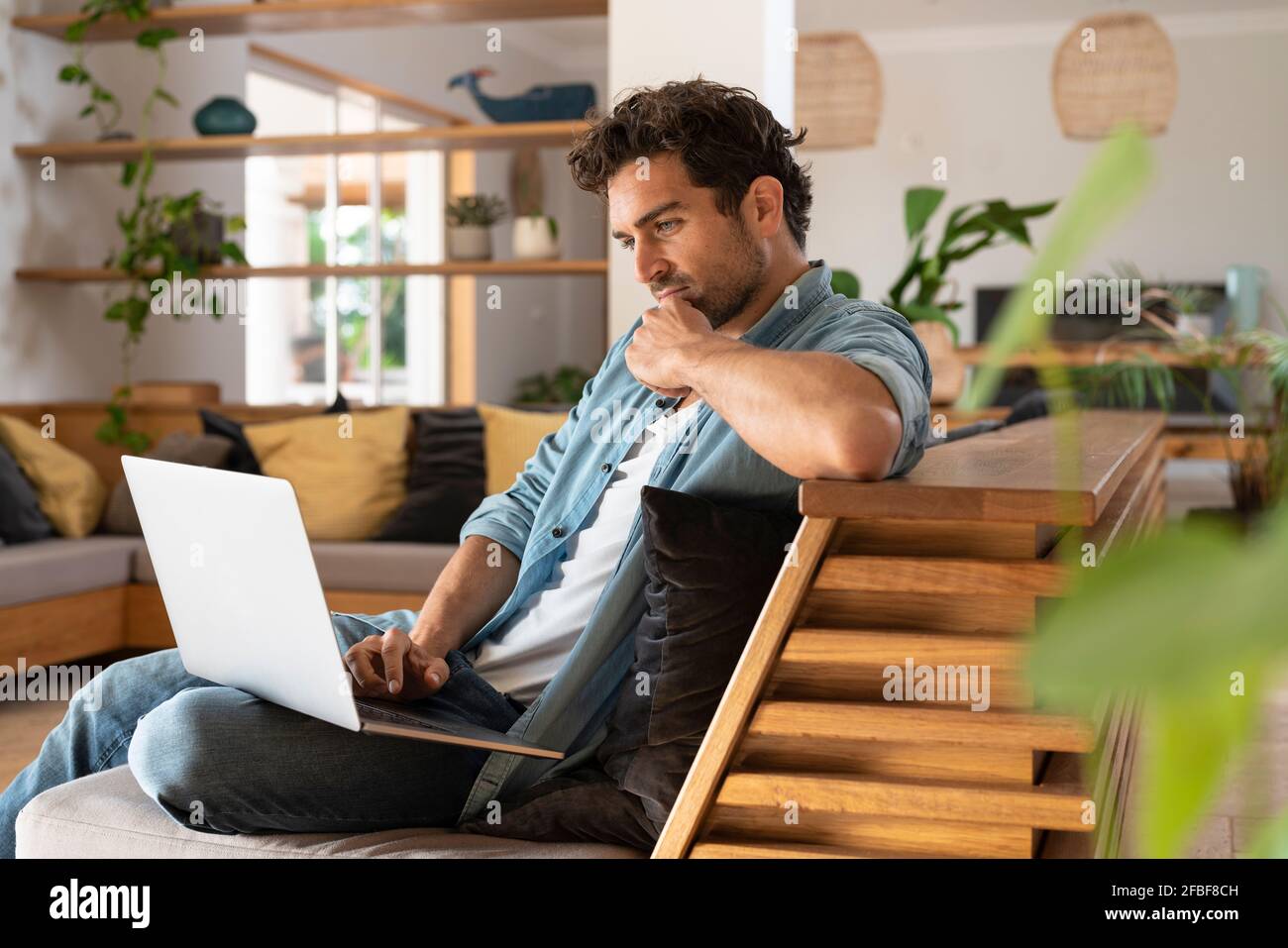 Travailleur indépendant concentré utilisant un ordinateur portable assis sur un canapé accueil Banque D'Images